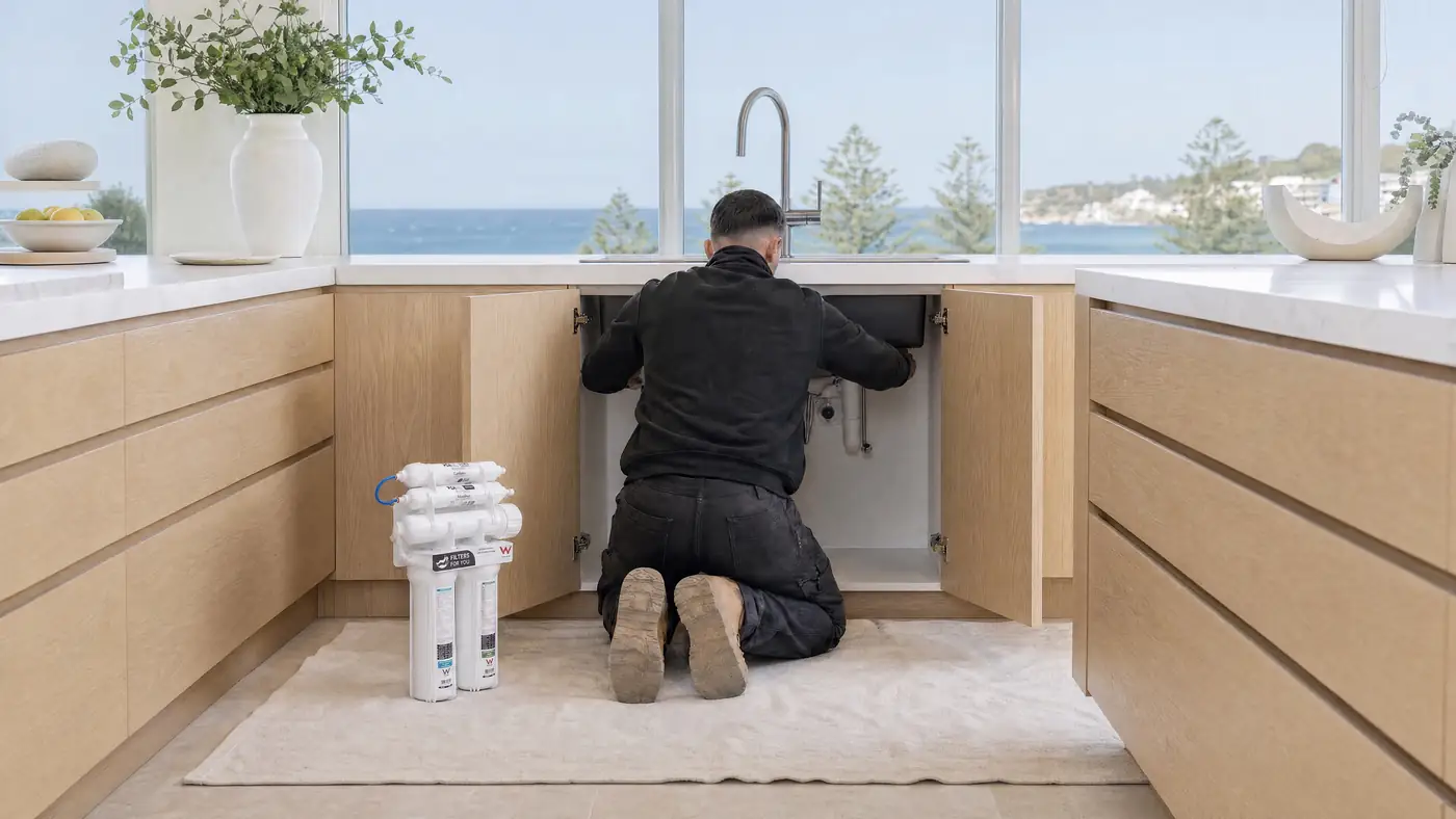 A Filters For You plumber at work in a Sydney kitchen, illustrative