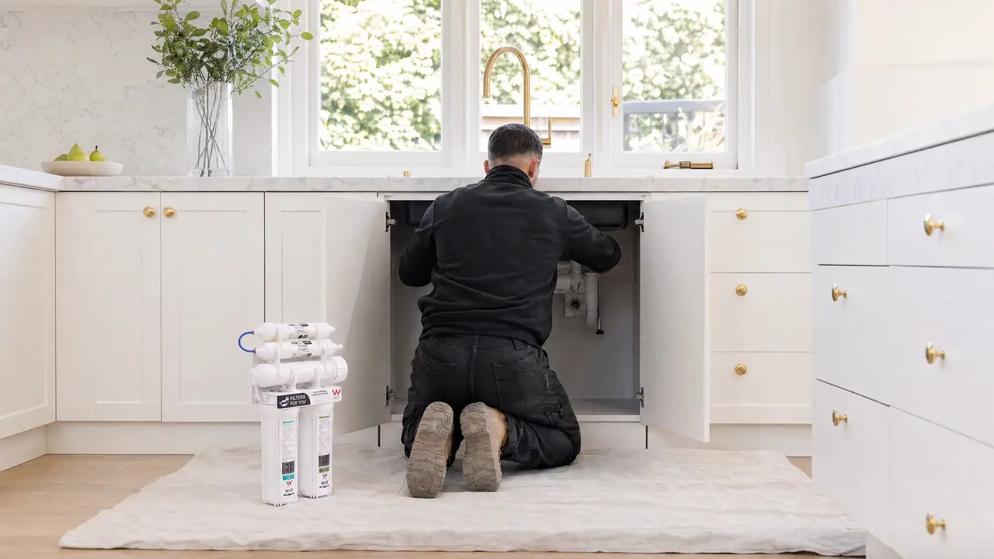 A Filters For You plumber at work in a Sydney kitchen, illustrative
