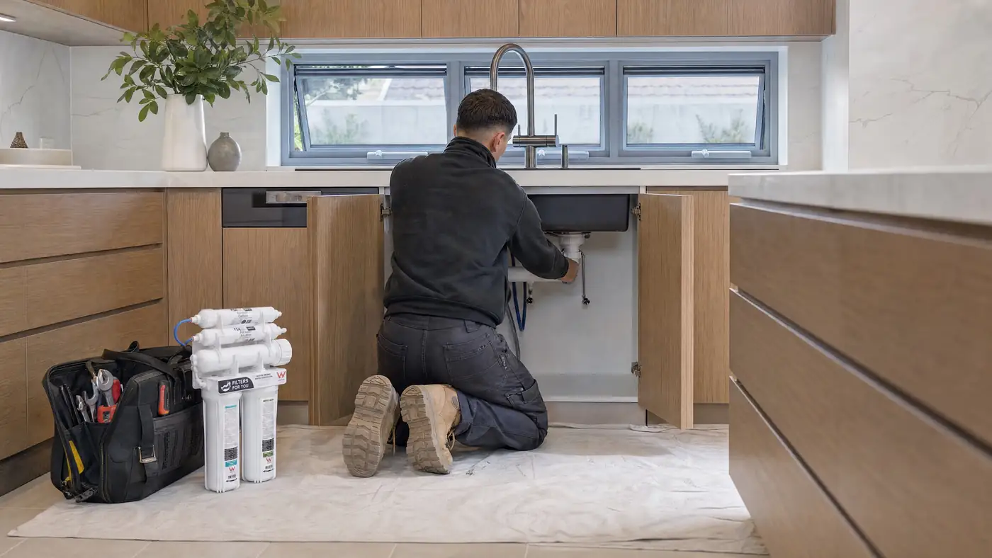 A Filters For You plumber at work in a Sydney kitchen, illustrative