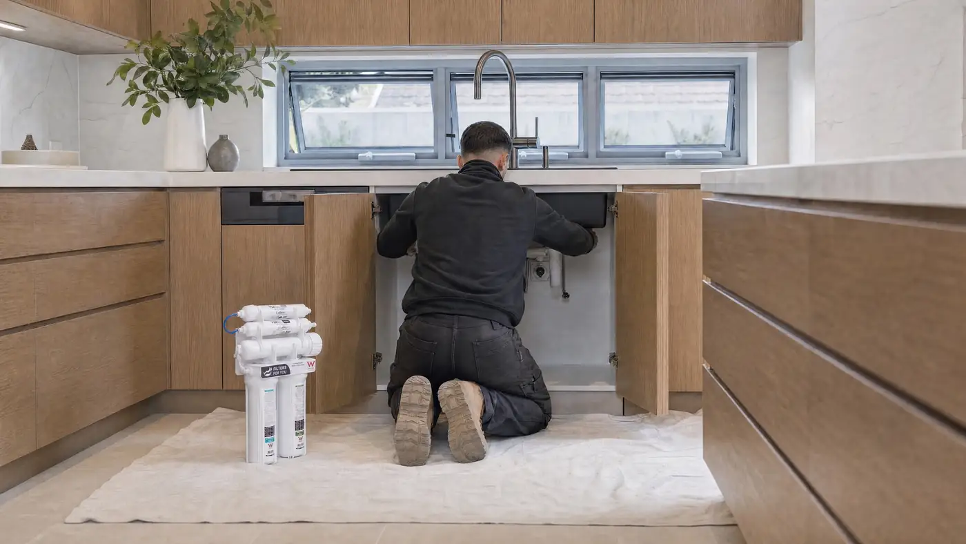 A Filters For You plumber at work in a Sydney kitchen, illustrative