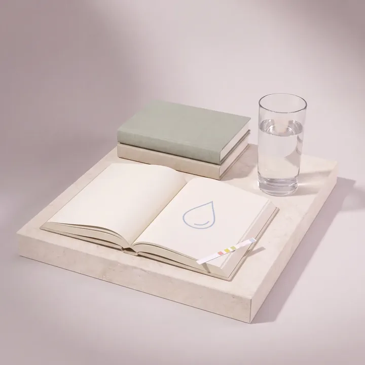 An open guide book with a water drop sketch beside a glass of water