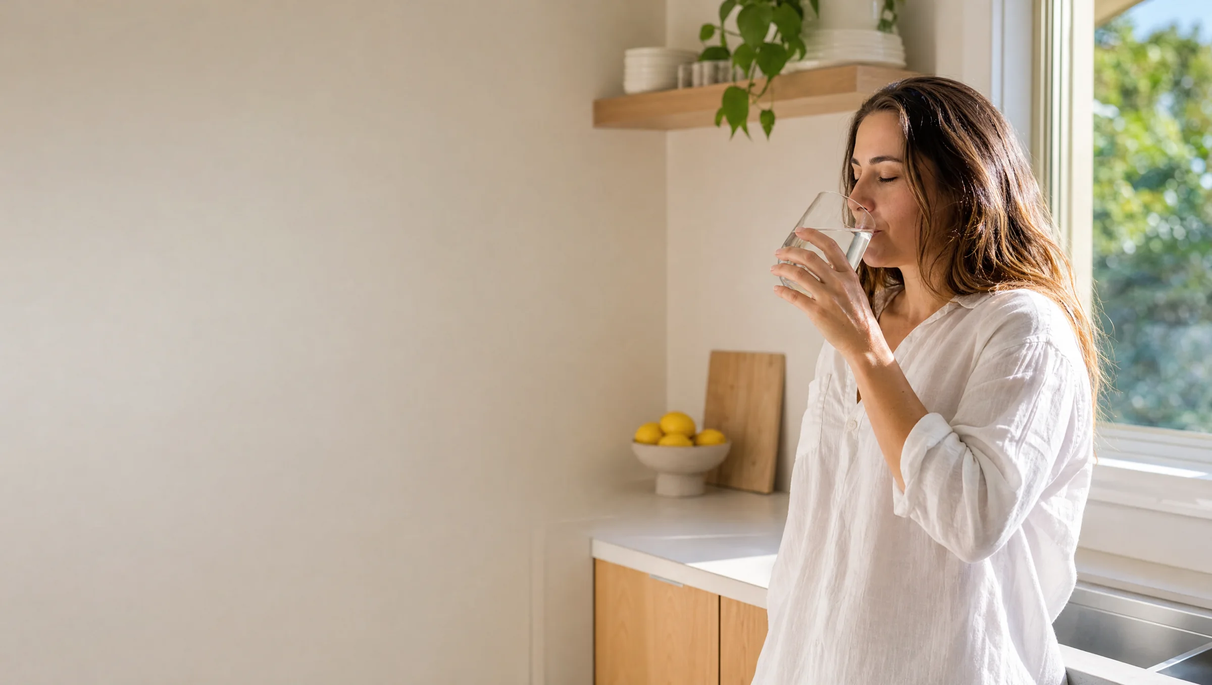 A woman drinking a glass of water by a bright window in her Sydney home