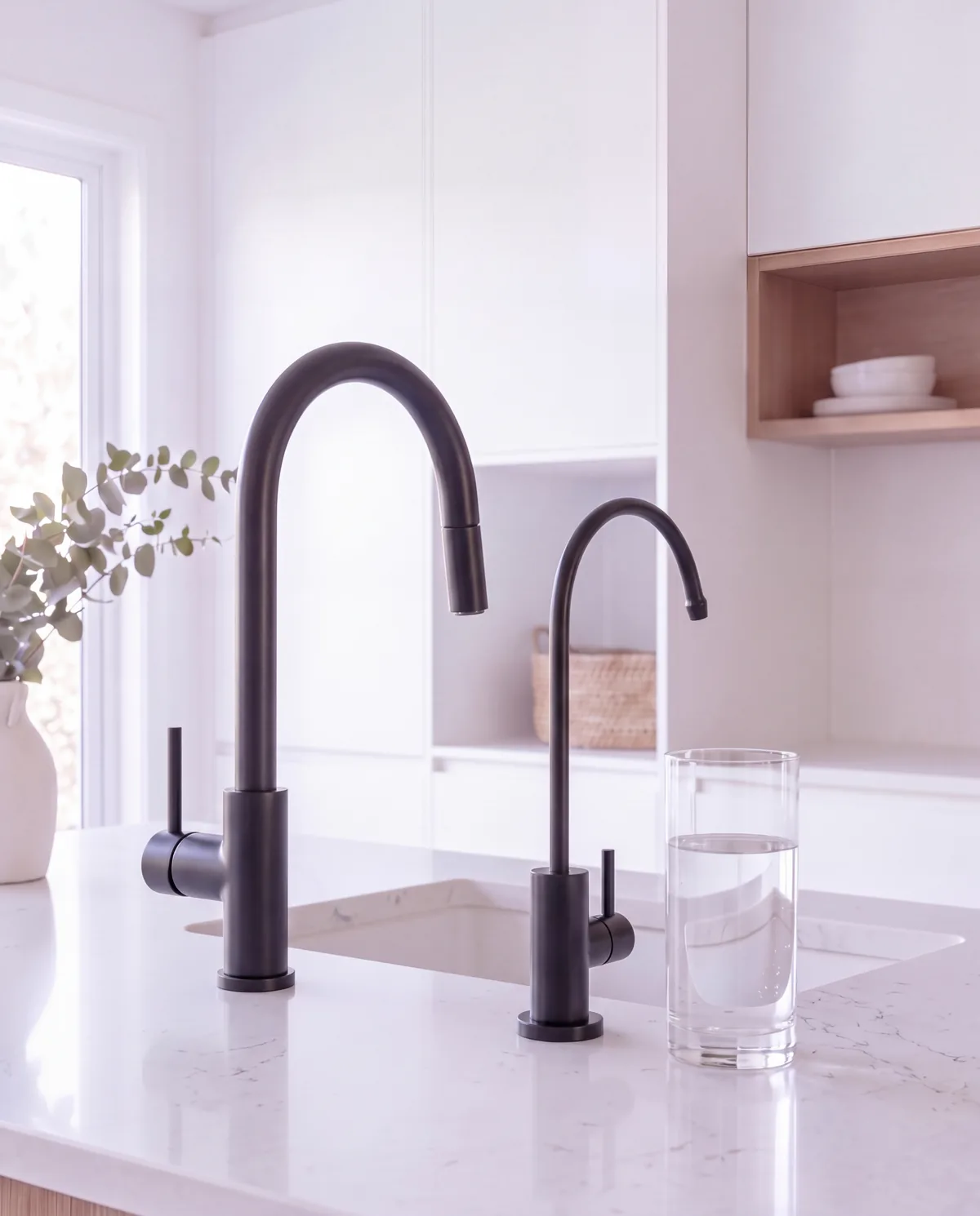 A slim matte black dedicated filtered water tap beside a matte black kitchen mixer on a white stone bench