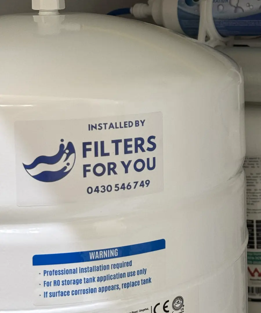 An Installed by Filters For You sticker with our phone number on a storage tank under a kitchen sink