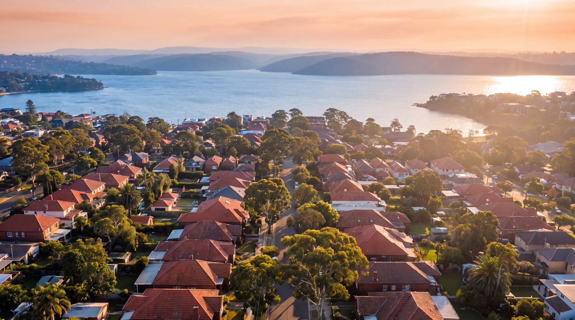 Red roofs of Sydney suburbs running down to the harbour at sunset